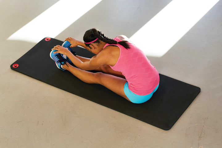 Woman does a forward fold stretch on a black SPRI hanging mat