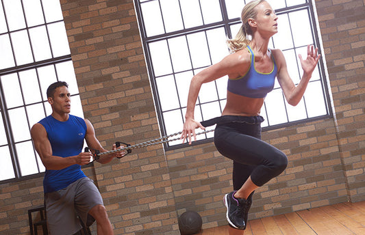 woman works out with exercise band with trainer at gym